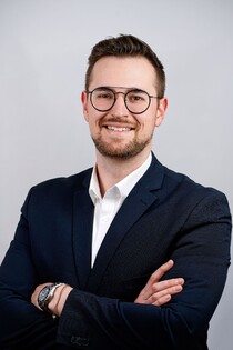 Porträtfoto eines Teammitglieds der Reisewelt Fröhlich mit Brille und Anzug.